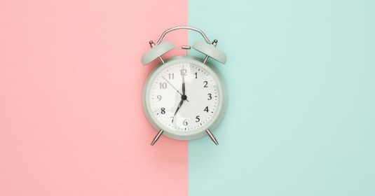 A white alarm clock on a split pink and blue backdrop
