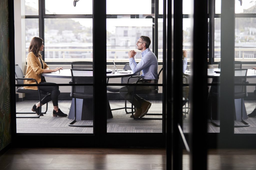 A man and woman having a conversation at a conference room table in an office