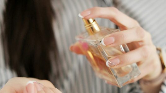 Woman with long dark hair spraying perfume on her wrist