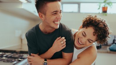 Nonbinary couple laughing and embracing in a kitchen
