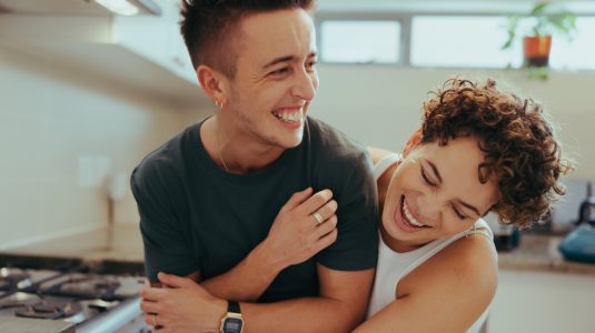 Nonbinary couple laughing and embracing in a kitchen